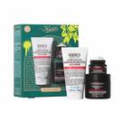 A graphic featuring a dark teal Kiehl’s gift box with white and gold accents on the left. The box contains three products. To the right of the box, the same three products are displayed outside of the box: a white tube of "KIEHL’S ULTRA FACIAL BARRIER-HYDRATING CLEANSER," a small black and red jar of "KIEHL’S AGE DEFENDER EYE REPAIR," and a larger black and red jar of "KIEHL’S AGE DEFENDER CREAM MOISTURIZER." The box is decorated with bright green graphic paint splatters and a bow design and features the text "YOUTH STILL GOT IT" at the bottom.
