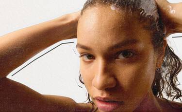 Close- up of a woman with wet, curly hair looking directly at the camera while rinsing her hair, illustrating Kiehl’s haircare and personal care products.​