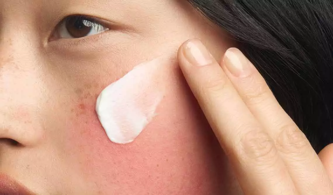 Action shot of the Kiehl's Ultra Facial Barrier-Hydrating Cleanser in use. The image shows the cream-to-foam formula creating a rich lather as it is massaged into the skin, demonstrating a gentle and refreshing cleansing experience.