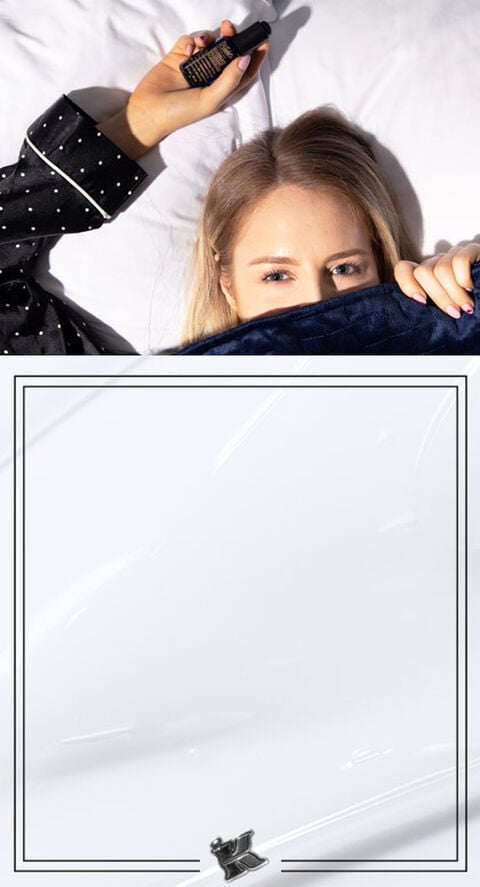 A woman lying in bed holding Midnight Recovery Oil from Kiehl's.