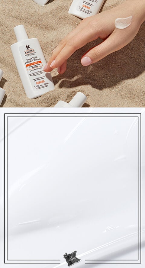 A persons hand digging into sand surrounded by Kiehl's sunscreen.
