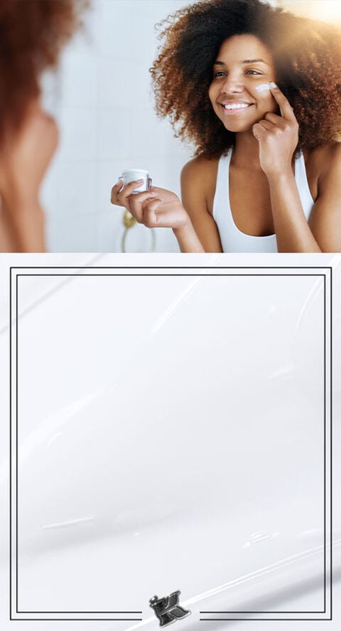 A person standing in a mirror putting a lotion onto their face.