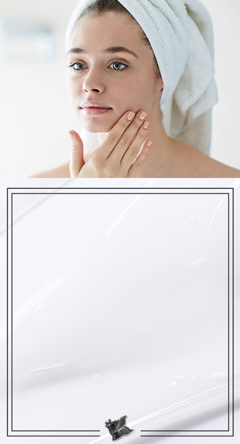 A woman with her hair wrapped in a towel touching her face.