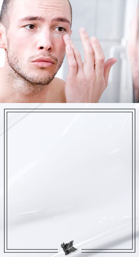 A man in a bathroom mirror applying a cream under his eye.